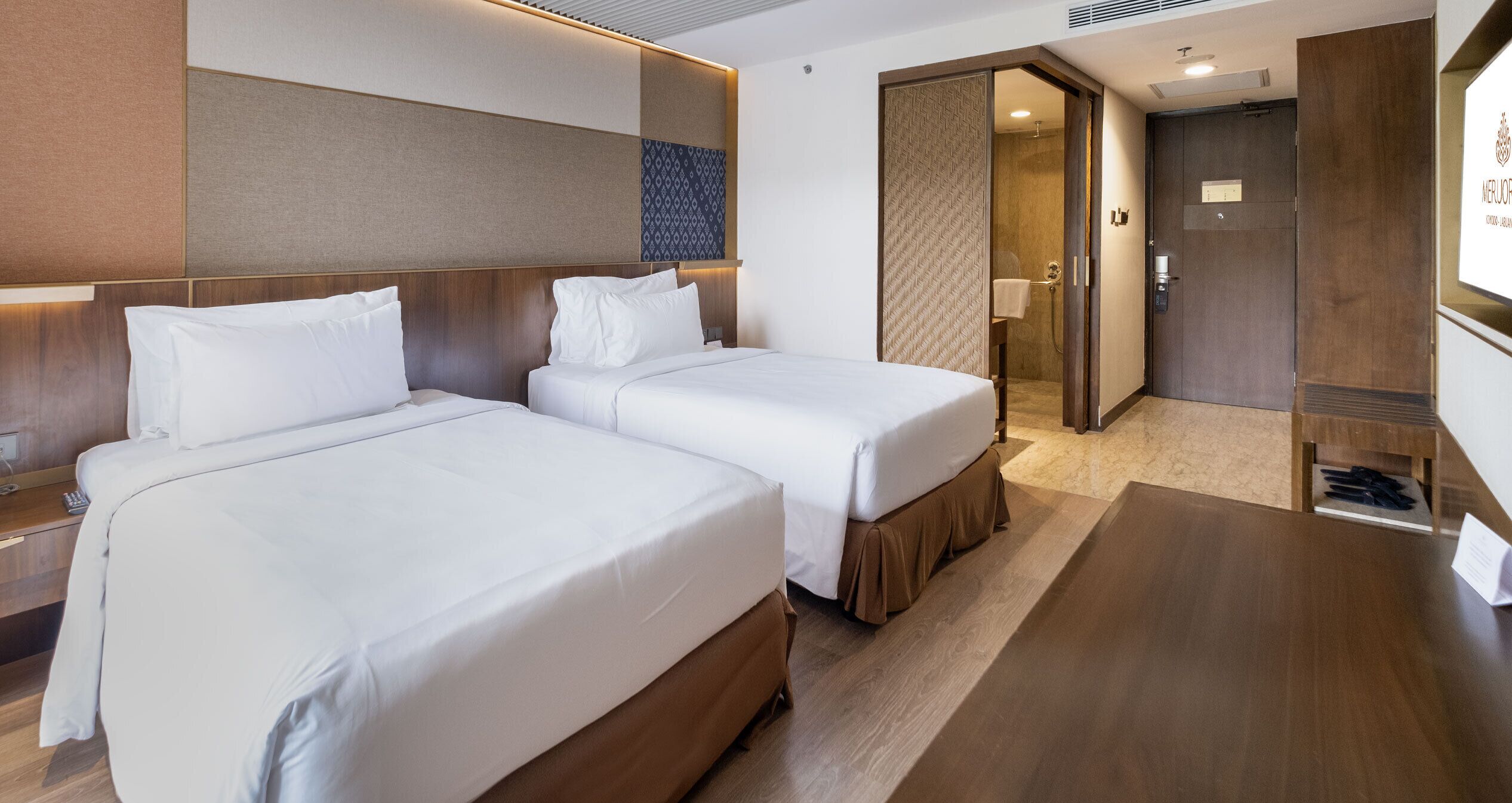 A hotel room with two beds, a wooden headboard, a small desk, and a mirror.