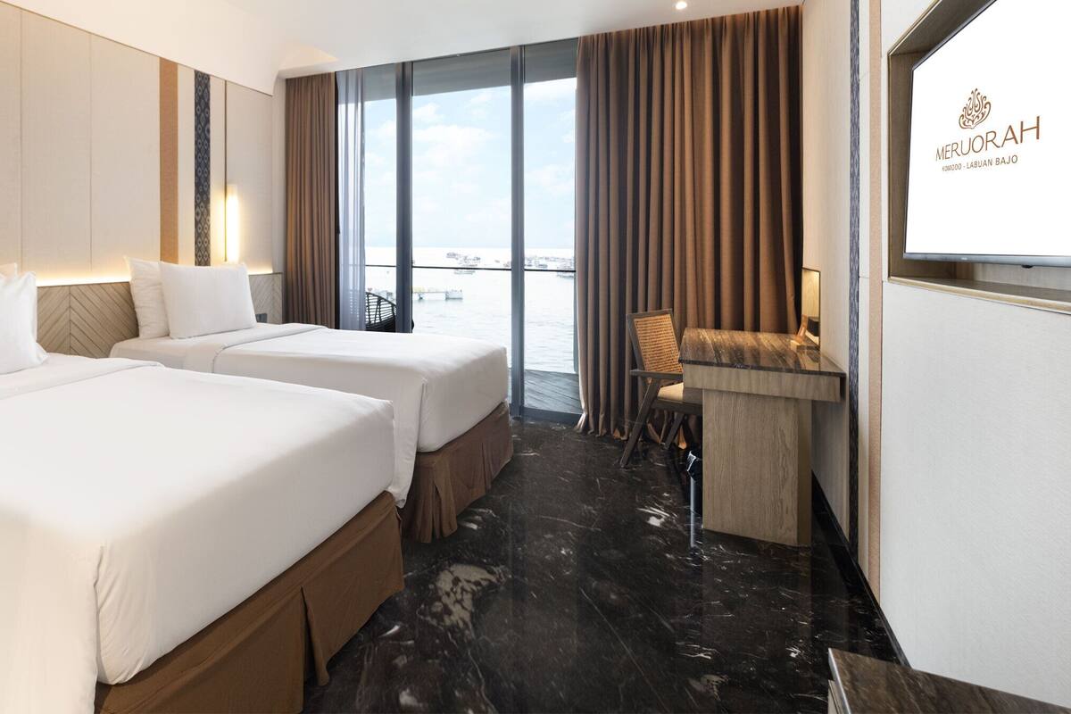 A hotel room with two beds, a desk, and a view of the water.