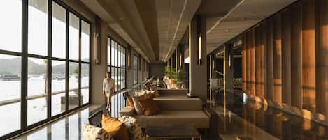 A spacious lobby with large windows, a seating area with sofas and cushions, and a view of a body of water.