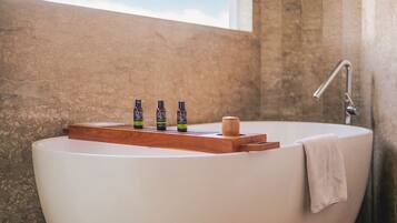 A bathtub with a wooden tray holding three bottles, a towel, and a window in the background.