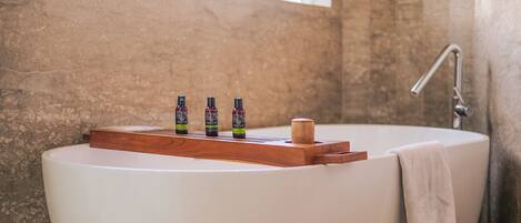 A bathtub with a wooden tray holding three bottles, a towel, and a window in the background.