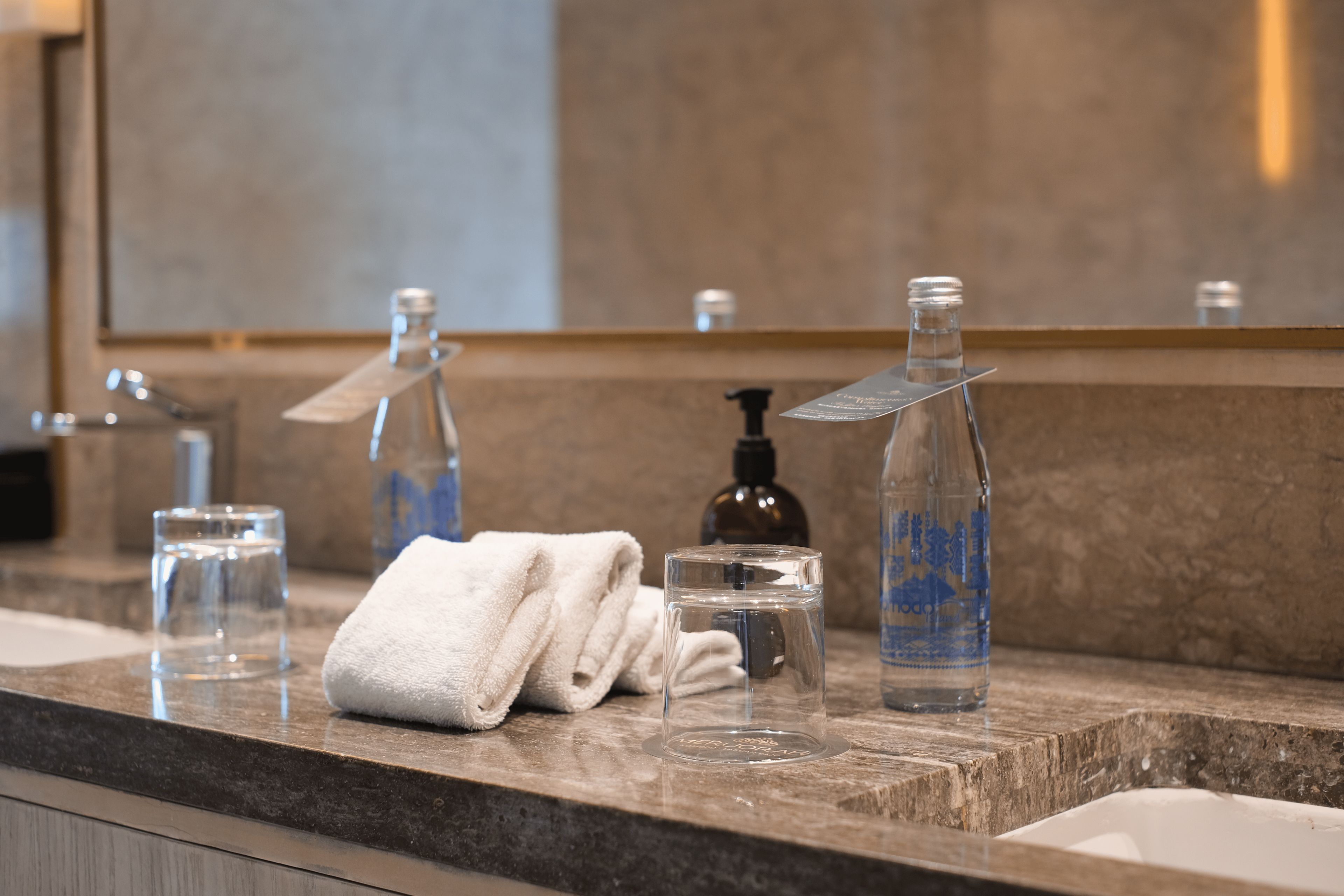 A bathroom counter with a towel, a glass, a soap dispenser, and a bottle.