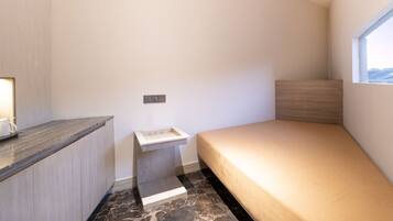 A small, modern room with a bed, a nightstand, a window, and a marble floor.