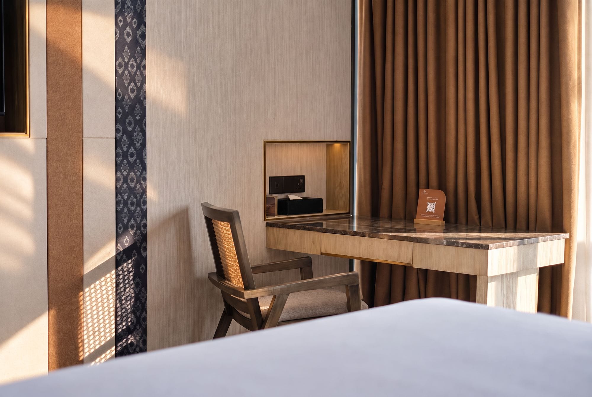 A hotel room with a bed, a desk with a chair, a mirror, and a curtain.