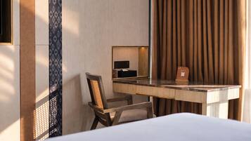 A hotel room with a bed, a desk with a chair, a mirror, and a curtain.