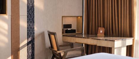 A hotel room with a bed, a desk with a chair, a mirror, and a curtain.