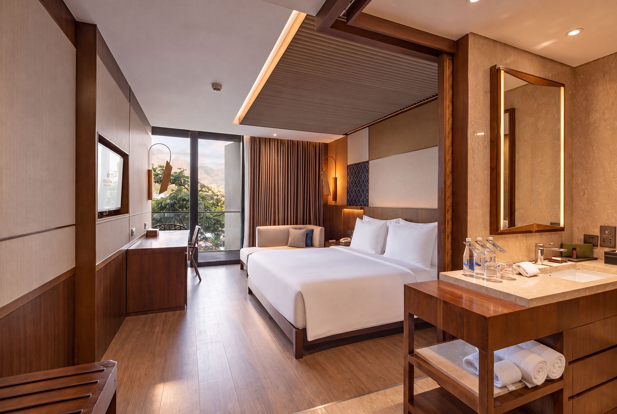 A hotel room with a bed, bedside table, mirror, and a view of the outdoors.