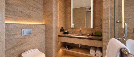 Un baño moderno con pared de mármol, un espejo grande, un lavamanos, un inodoro y una cabina de ducha de vidrio.