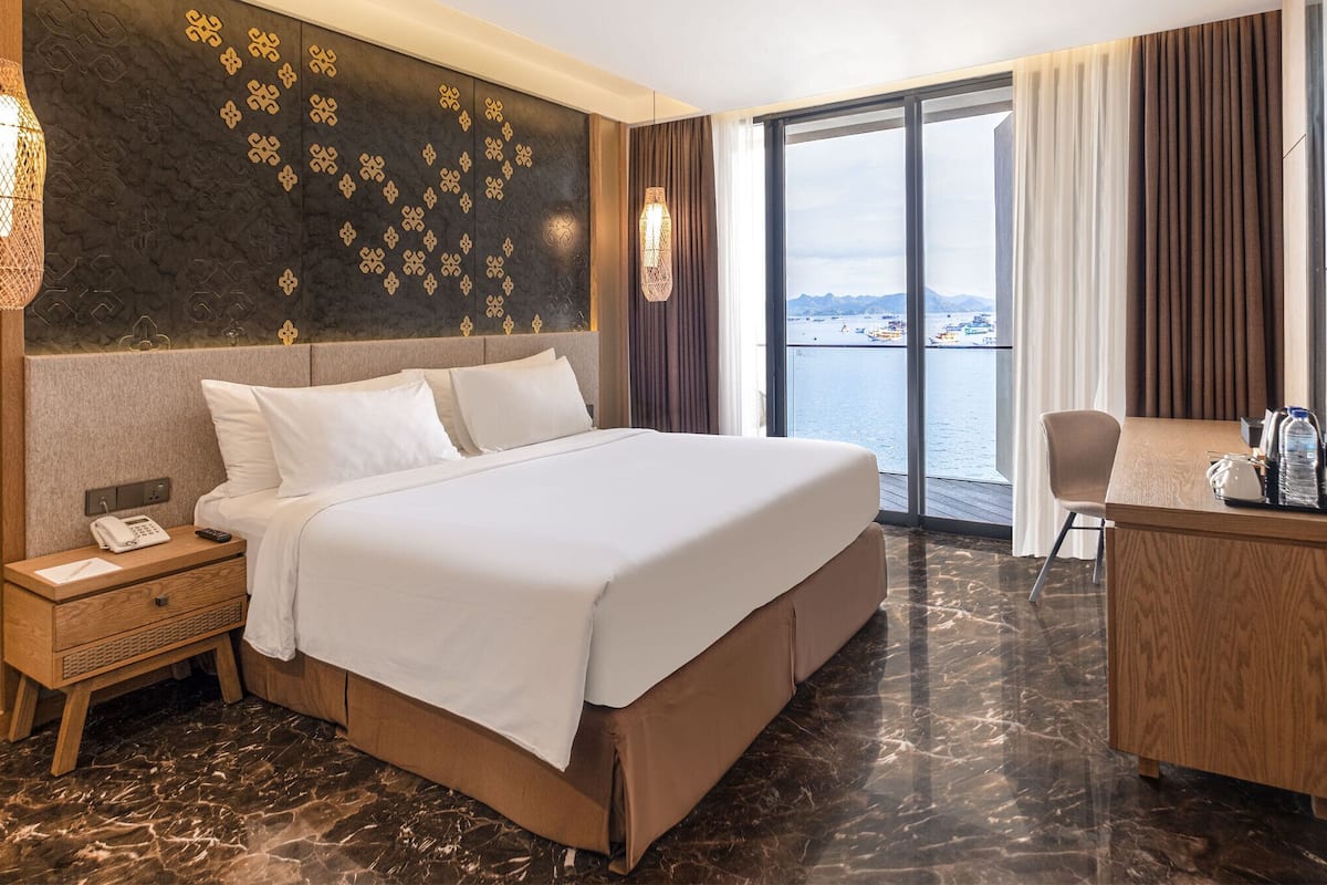 A hotel room with a large bed, a desk, and a view of the sea.