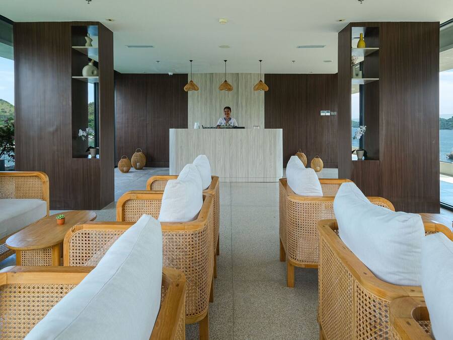 A modern reception area with wicker furniture, a wooden reception desk, and large windows offering a view of the sea and hills.