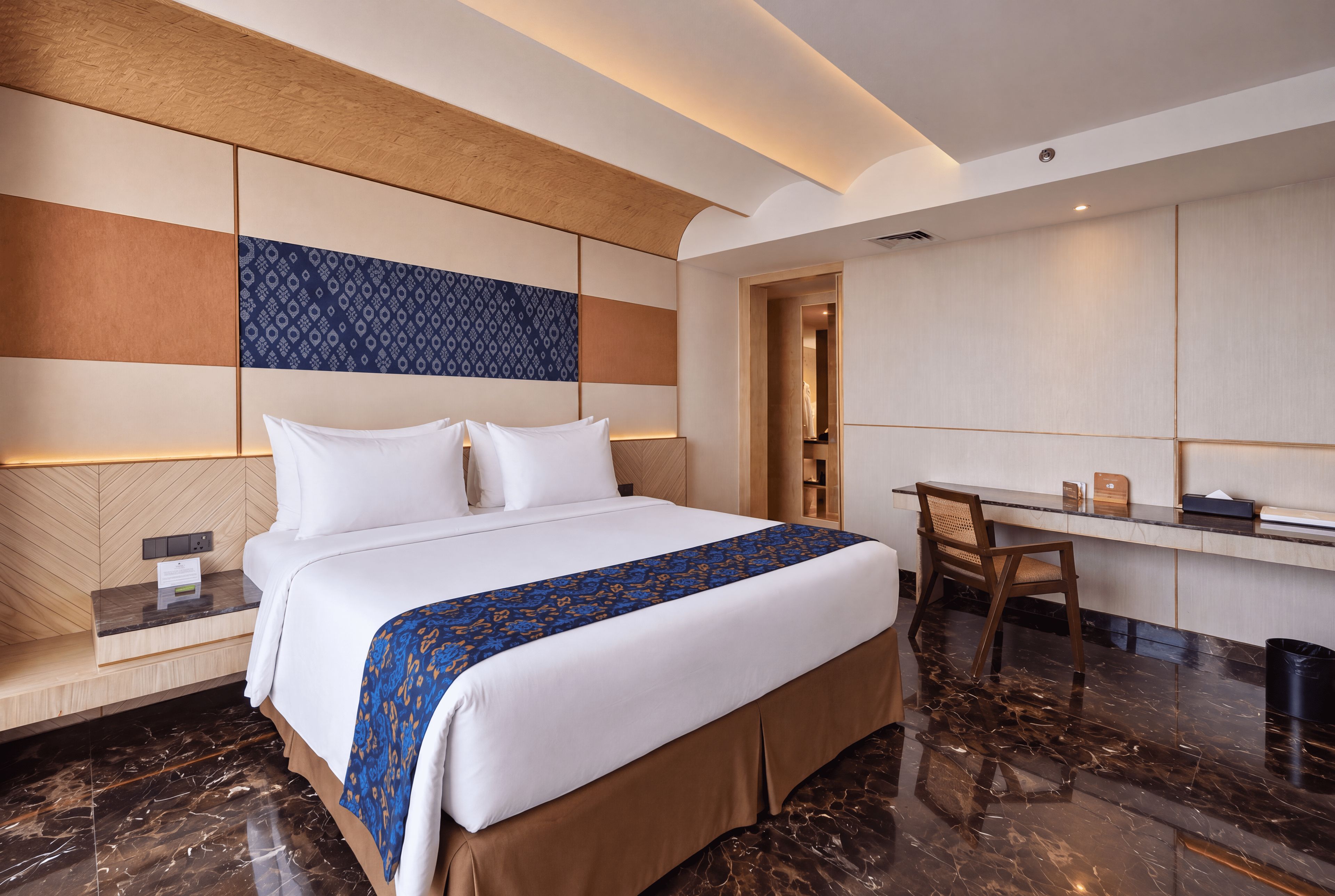 A modern hotel room with a large bed, a desk, and a seating area.