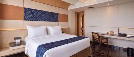 A modern hotel room with a large bed, a desk, and a seating area.
