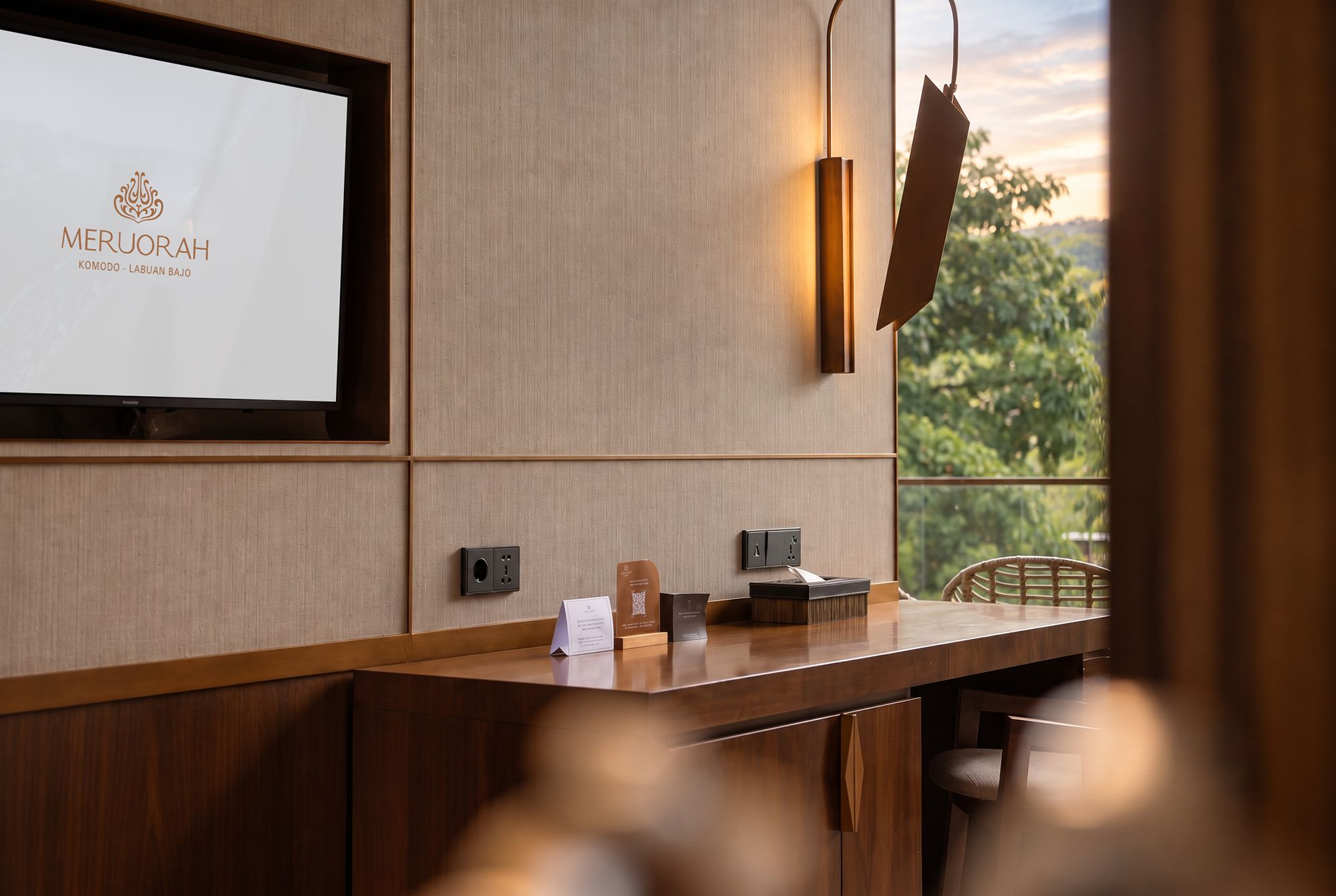 A reception desk with a framed sign, a wall-mounted light fixture, and a view of greenery outside.