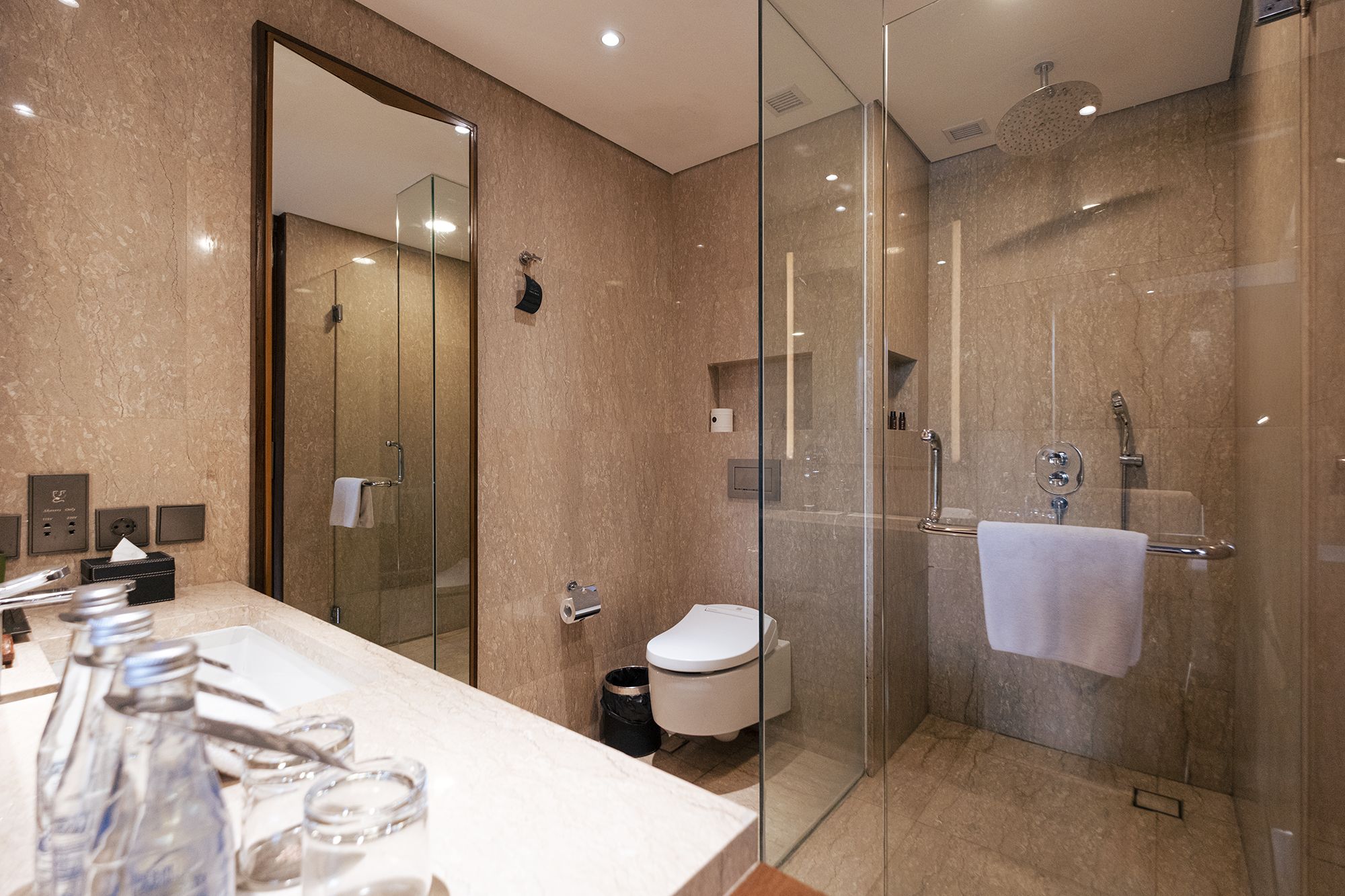 A modern bathroom with a glass-enclosed shower, a toilet, and a sink with toiletries.