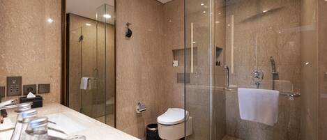 Un baño moderno con ducha de vidrio, inodoro y lavamanos con artículos de aseo.
