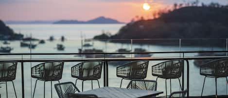 A terrace with outdoor seating and a view of the sea at sunset.