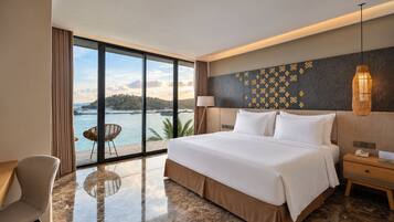 A hotel room with a large bed, a desk, a chair, and a view of the sea.