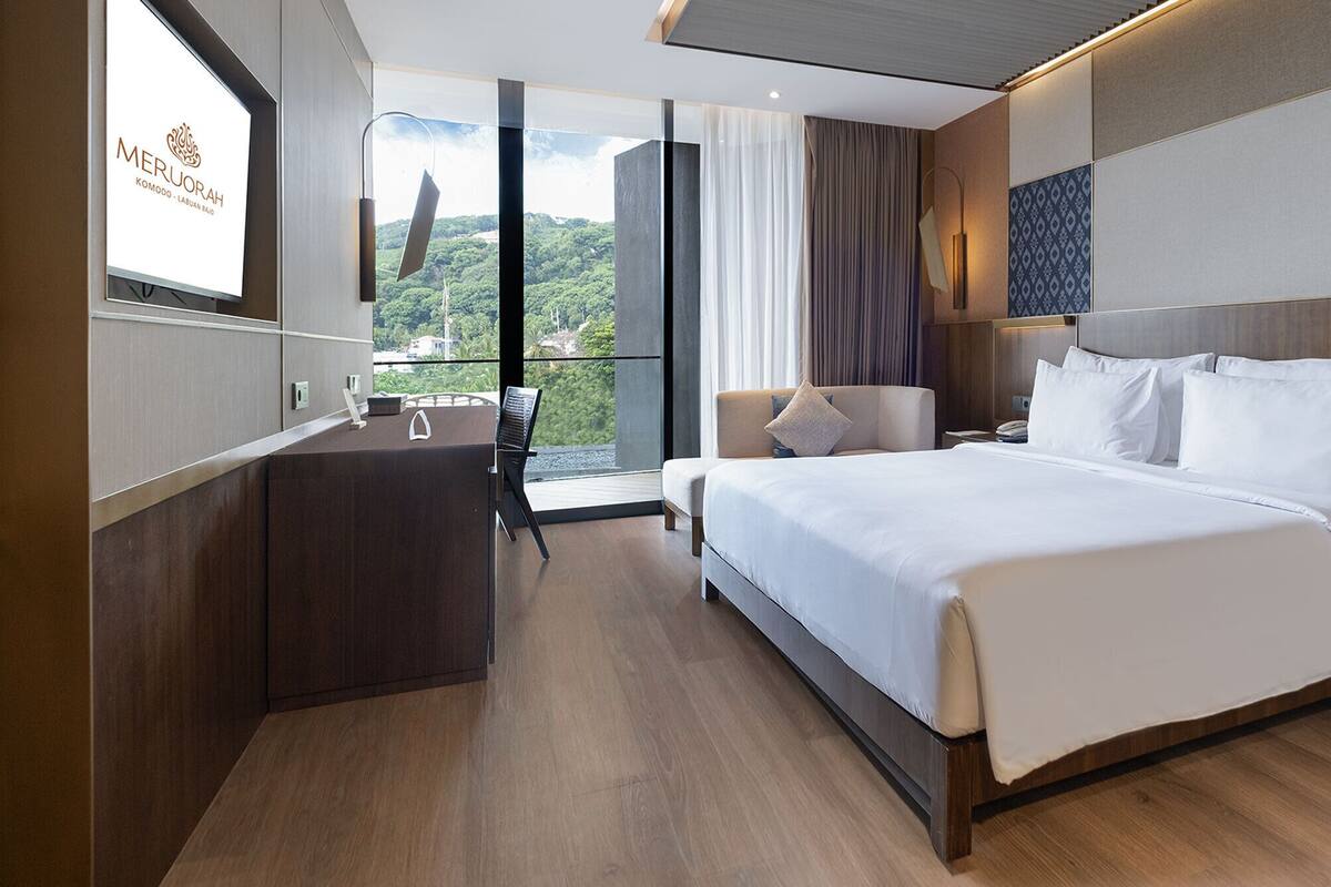 A modern hotel room with a large bed, a desk, and a view of the outdoors.