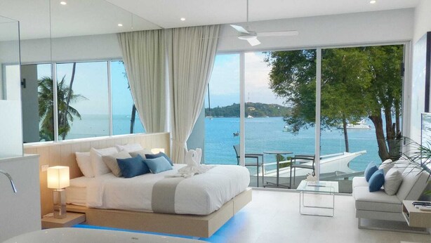 A modern hotel room with a large bed, a bathtub with rose petals, a balcony with a view of the sea, and a seating area with a table and chairs. - FREE $1600 Daily Luxury Pack - 16-Bed Beachfront Villa - Private Pool, Spa & Gym (Tambon Vichit, Ampur Muang)