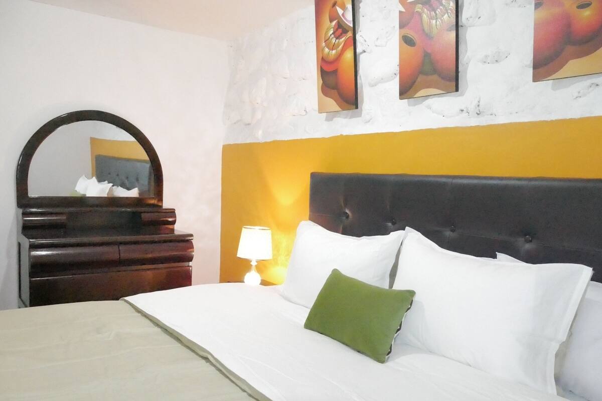 A hotel room with a bed, a dresser, a mirror, and wall art.