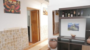 A hallway with a stone wall, a wooden door, a shelf with bottles, and a painting. - Cusco Dulce House Apartment (Cusco)