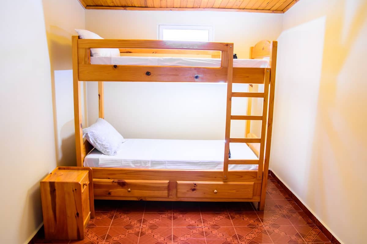 A bunk bed with a ladder, a small wooden bench, and a window.