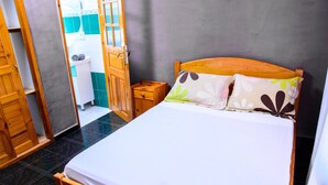 A bedroom with a wooden bed, two pillows, a nightstand, and a bathroom visible through an open door. - Hotel Restaurant Azalee (Antananarivo)