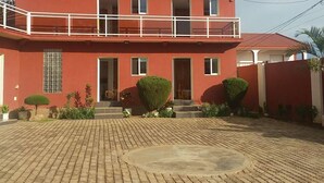 A multi-story building with a red facade, balconies, and a paved courtyard. - Hotel Restaurant Azalee (Antananarivo)