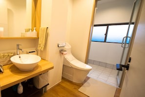 A modern bathroom with a large sink, toilet, and a glass shower door leading to a balcony with a view. - N House (Nago)