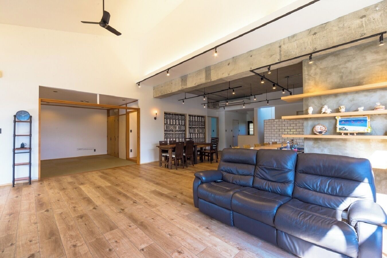A spacious living area with a wooden floor, a leather sofa, a dining table, and a kitchen area with a brick backsplash.