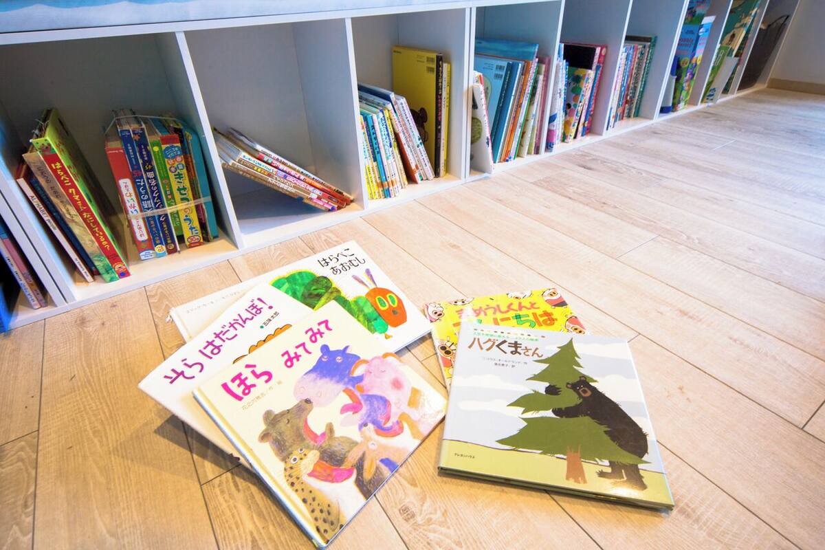 A bookshelf with various books and a few books on the floor.
