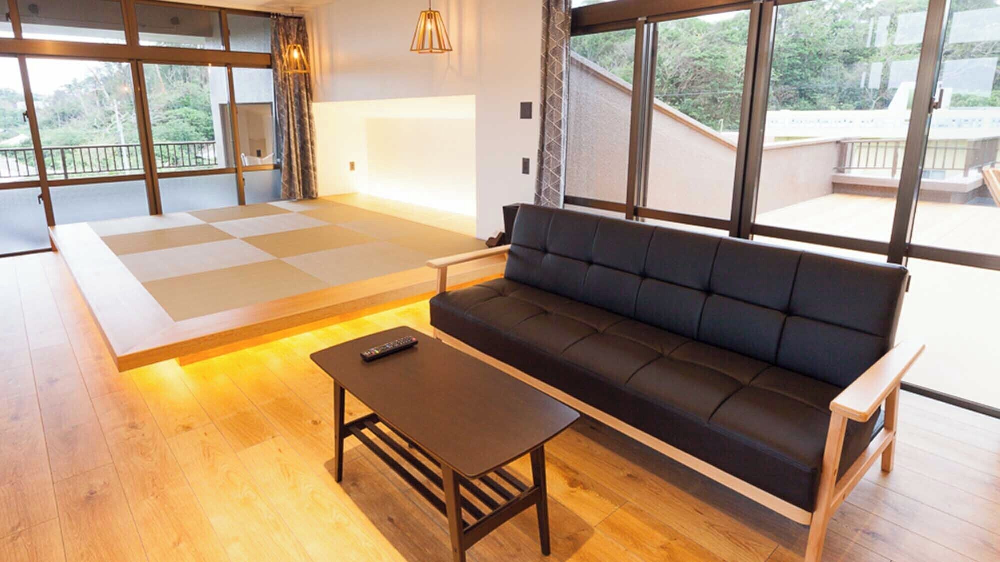 A modern living room with a sofa, a coffee table, and a tatami mat area.