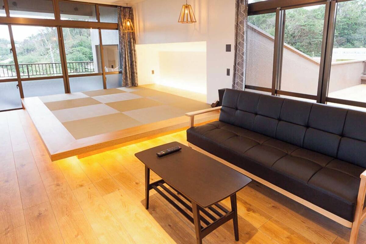 A modern living room with a sofa, a coffee table, and a tatami mat area.