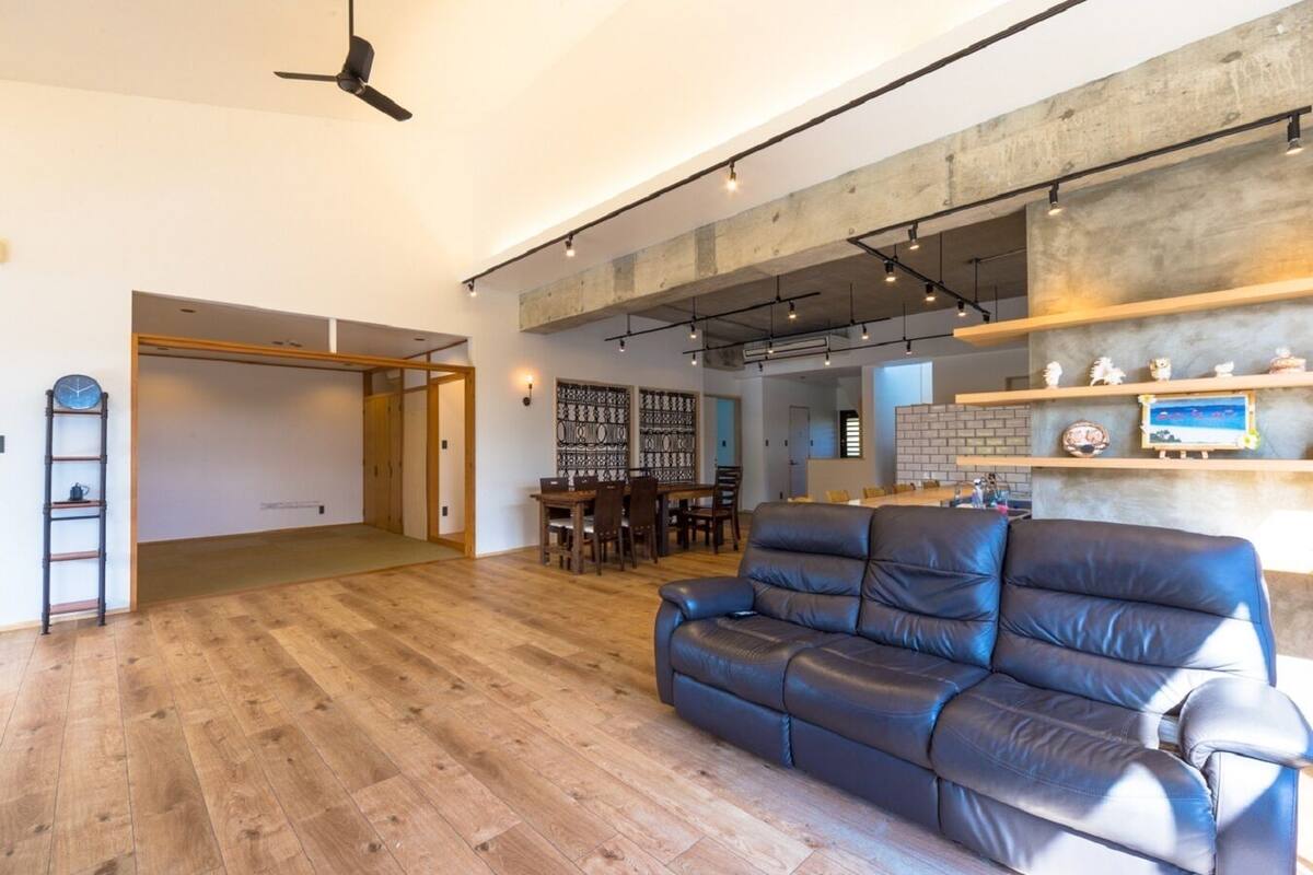 A spacious living area with a wooden floor, a leather sofa, a dining table with chairs, and a kitchen area with a brick backsplash.