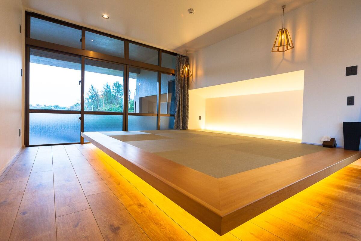 A modern room with a large bed, a view through large windows, and a unique lighting feature along the bed's edge.