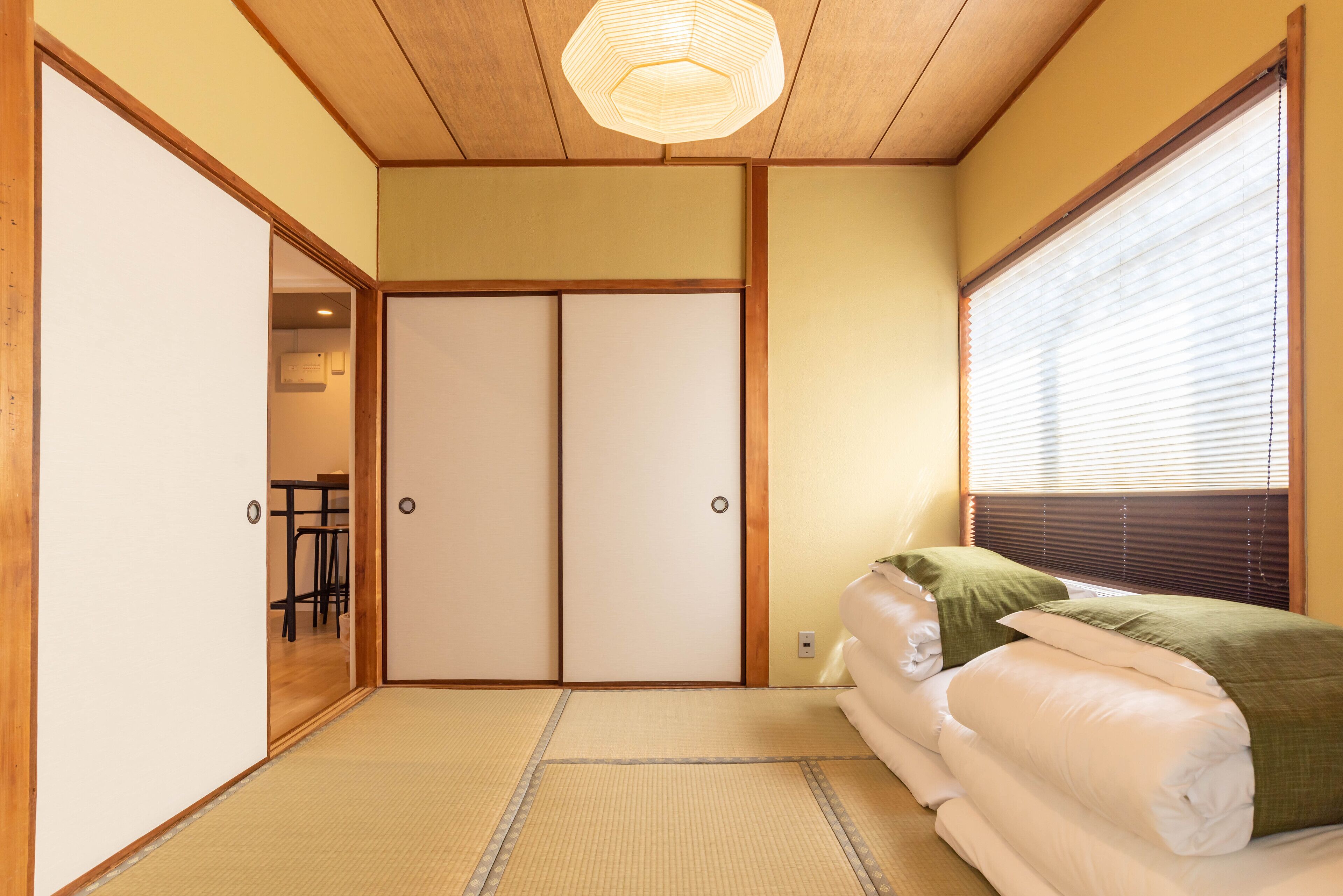 A traditional Japanese room with tatami flooring, a sliding door, and a bed with green pillows.