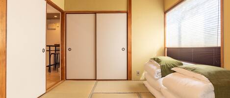 A traditional Japanese room with tatami flooring, a sliding door, and a bed with green pillows.