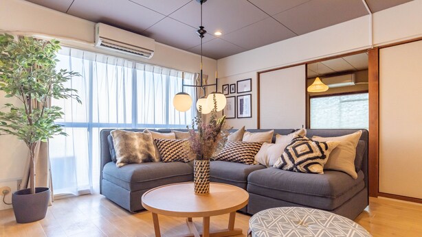 Ein modernes Wohnzimmer mit einem grauen Sofa, einem runden Holztisch und einer Topfpflanze.
