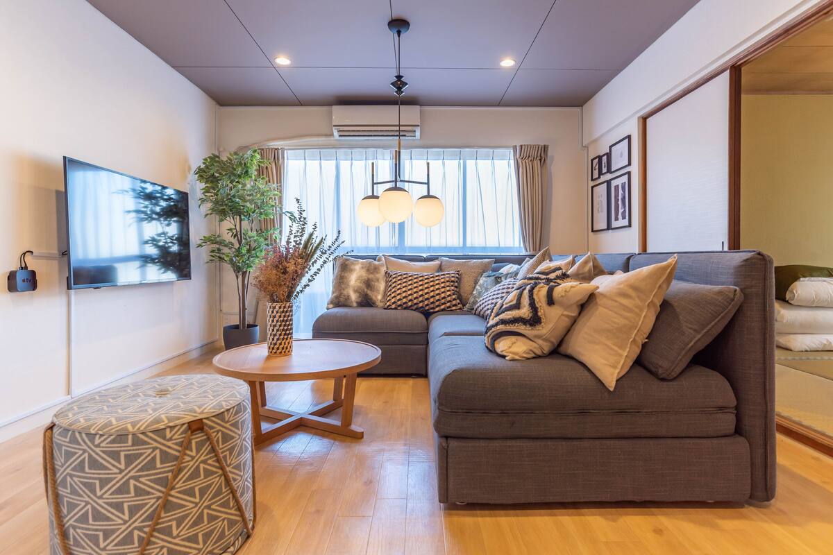 A modern living room with a grey sofa, a round wooden coffee table, and a patterned ottoman.
