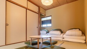Ein traditioneller japanischer Raum mit Tatami-Bodenbelag, einem niedrigen Tisch und Futonbetten mit Kissen.