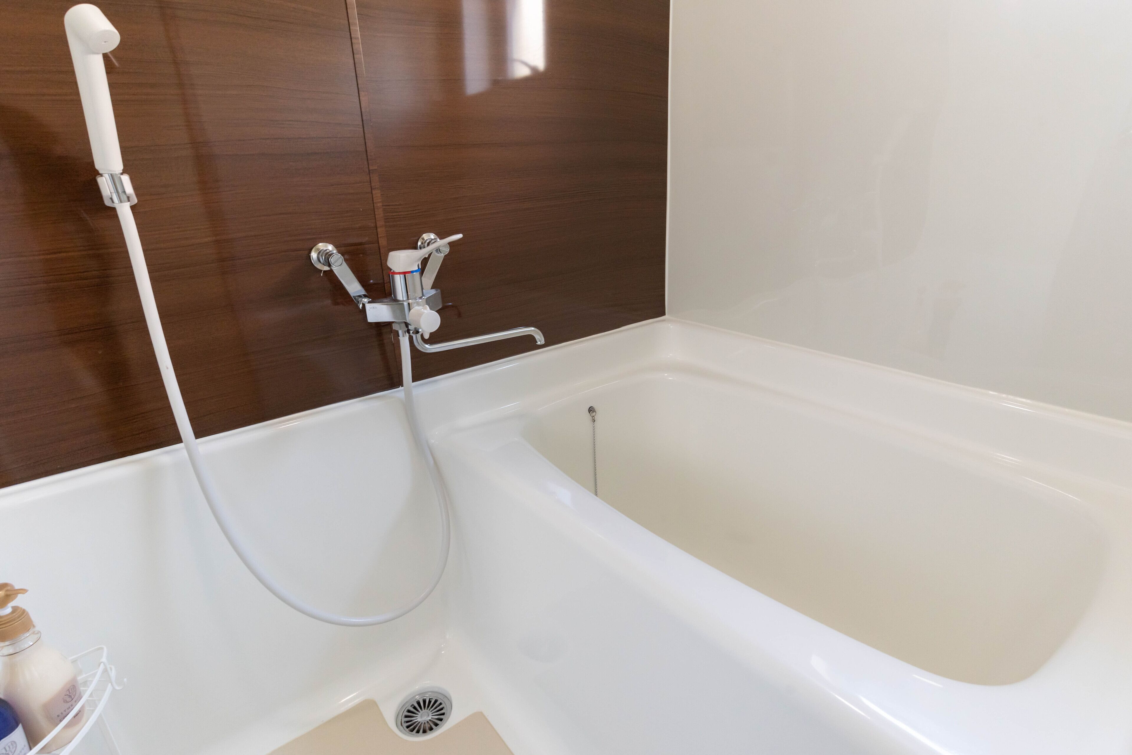 A white bathtub with a handheld showerhead and a wall-mounted faucet.