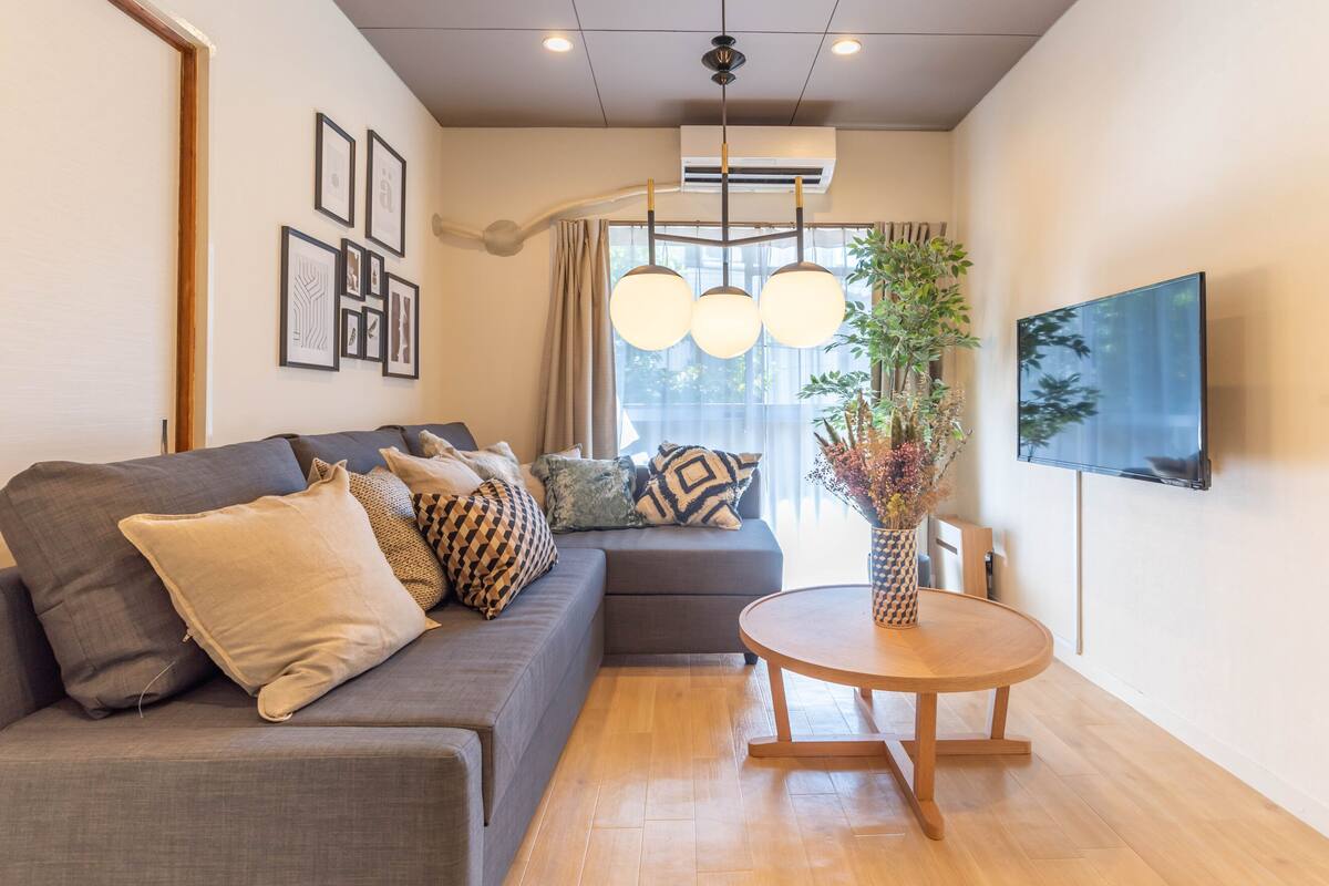A modern living room with a grey sofa, a round wooden table, and a mounted TV.