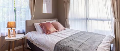A bedroom with a bed, a bedside table with a lamp, and a window with curtains.