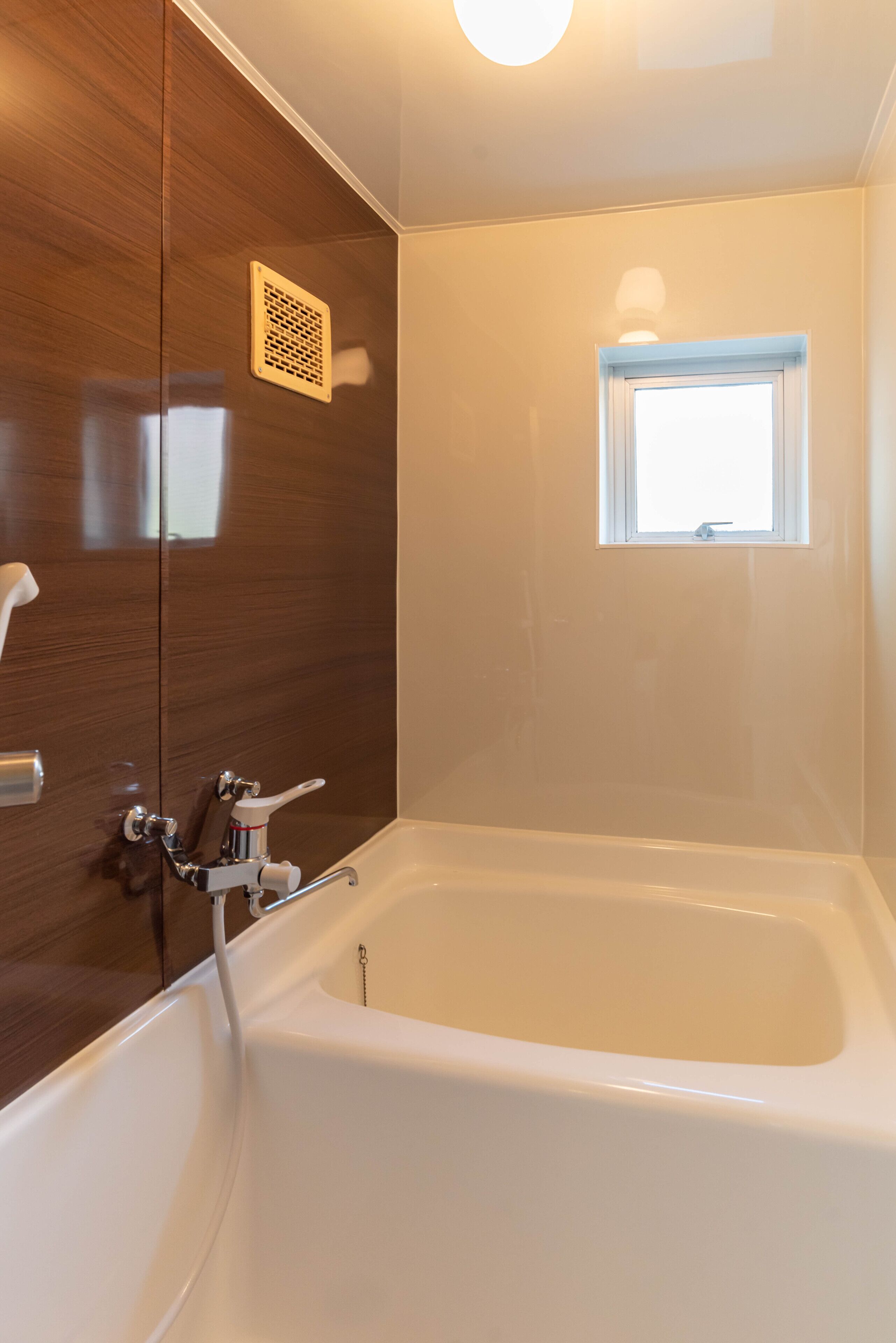 A modern bathroom with a bathtub, a window, and a wooden panel wall.