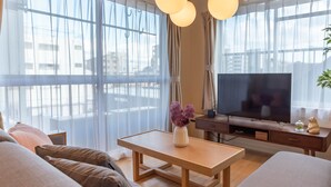 Ein modernes Wohnzimmer mit einer Couch, einem Couchtisch, einem Fernseher und einem großen Fenster mit durchsichtigen Vorhängen.