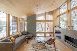 A modern living room with a large window, a grey sofa, a round glass table, and a fireplace. - Kairos by the Mountain (Hakuba)