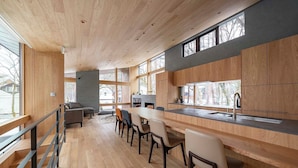 A modern kitchen with wooden cabinets, a bar area, and a dining space with chairs. - Kairos by the Mountain (Hakuba)