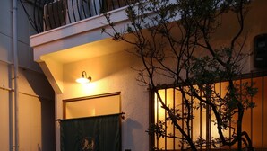 A two-story building with a balcony, a small tree in front, and a sign with Japanese characters.