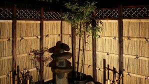 A serene garden with a bamboo fence, a stone water feature, and a variety of potted plants.