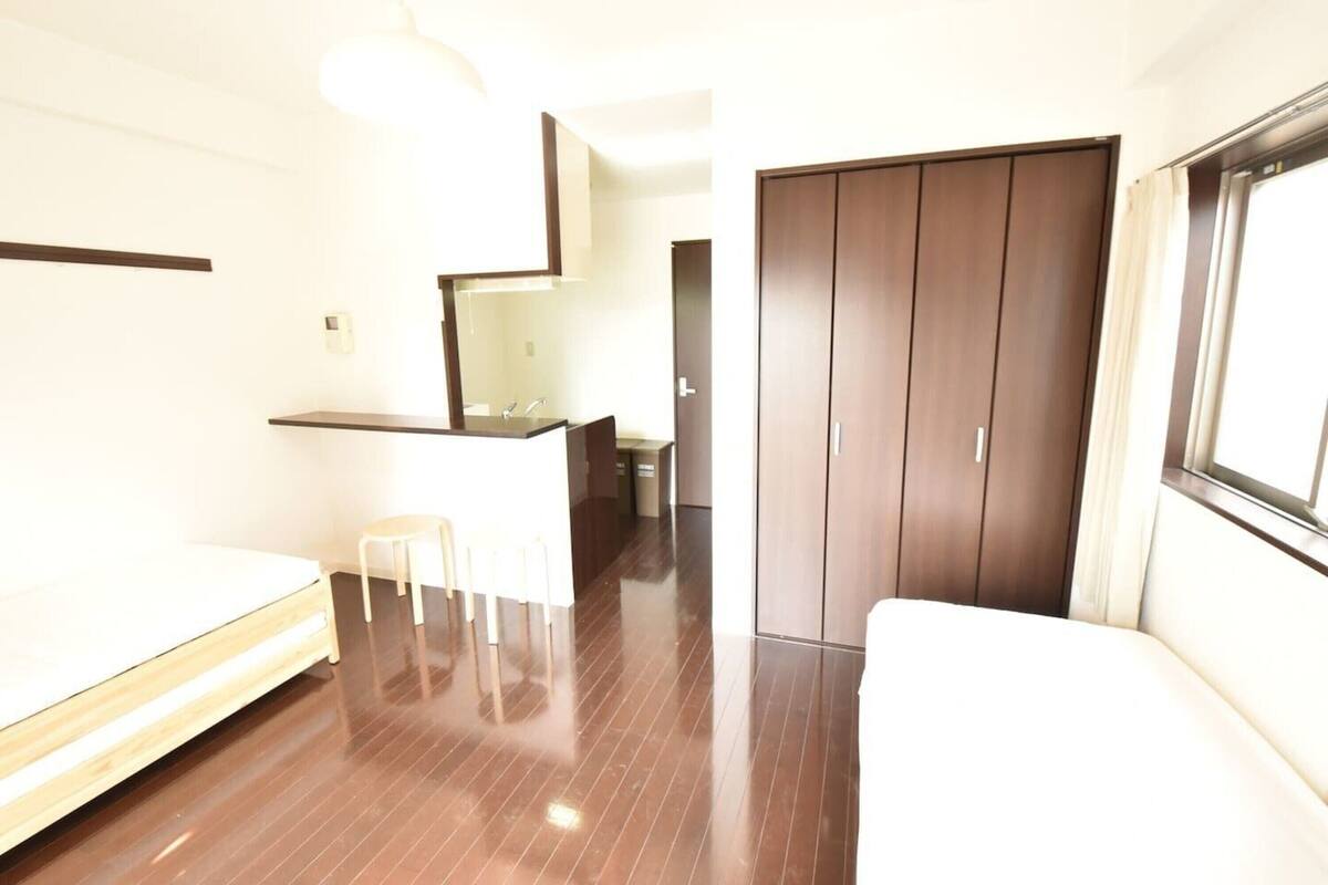 Habitación de hotel con cama, un taburete pequeño, un espejo, armario y ventana.